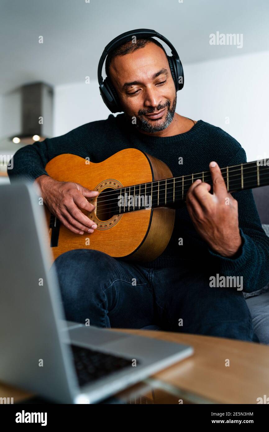 Entspannter Mann mittleren Alters spielt Gitarre zu Hause im Wohnzimmer Zimmer Stockfoto