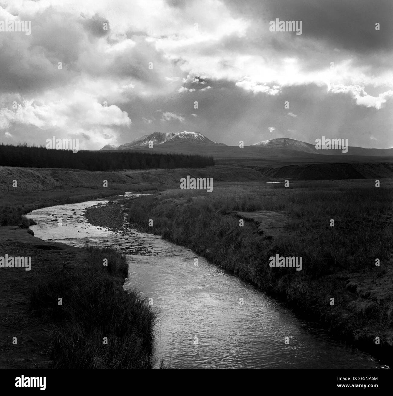 Schwarz und Weiß der Brecon Beacons Wales, Vereinigtes Königreich mit Schneedecke der Hügel mit launischen Himmel und Fluss im Vordergrund Stockfoto