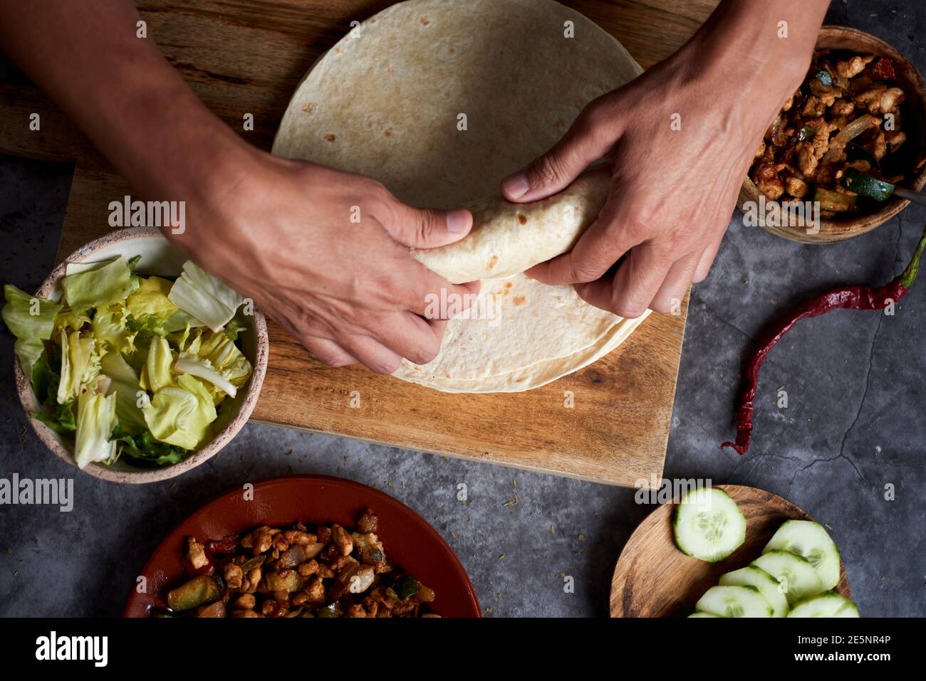Ein junger Kaukasusmann, von oben gesehen, rollt ein Durum oder ein Burrito, gefüllt mit Hühnerfleisch gekocht mit verschiedenen Gemüse wie Zwiebel oder rot und Stockfoto