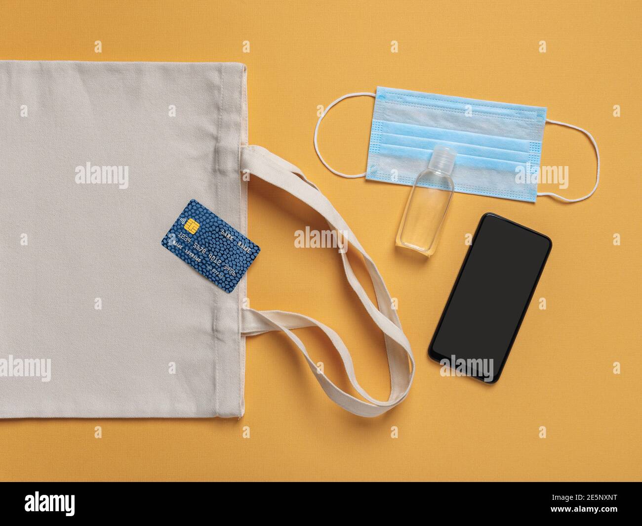 Kreditkarte auf Baumwolltasche, Smartphone, Handdesinfektionsmittel und Einweg-Gesichtsmaske auf gelbem Hintergrund. Schutz vor Kovid und Grippe. Speicherplatz kopieren. Stockfoto