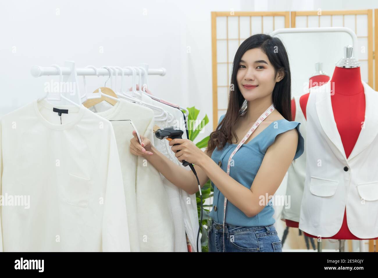 Small Business Owner Konzept. Junge glücklich zuversichtlich Designer asiatische Frau mit Band Maß am Hals verwenden Sie Handheld-Barcode-Scanner auf Kleidung zu schießen Stockfoto