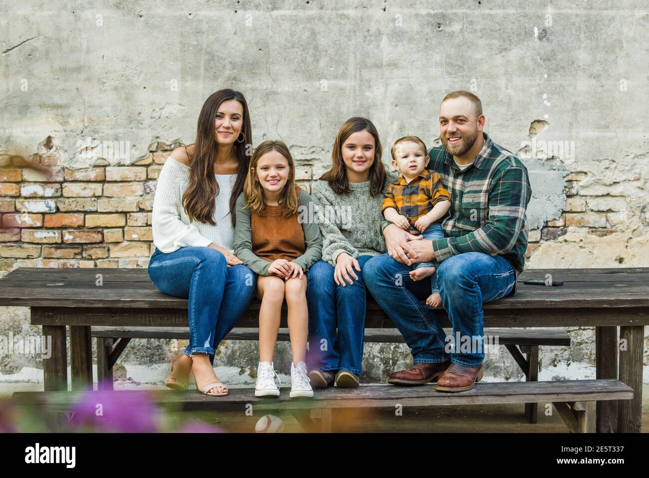 Blended Familie von fünf mit zwei Mädchen und ein Baby Junge sitzt auf einem Tisch an einem urban alten Backstein Wand Stockfoto