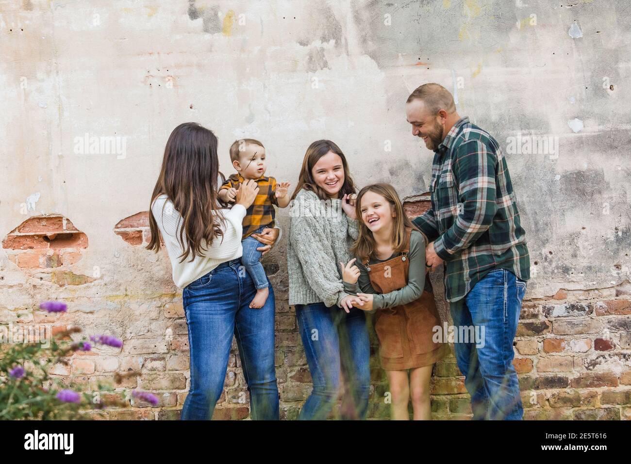 Eine fünfköpfige Familie mit zwei Mädchen und einem Baby Junge steht an einer urbane alte Ziegelmauer und lacht Stockfoto