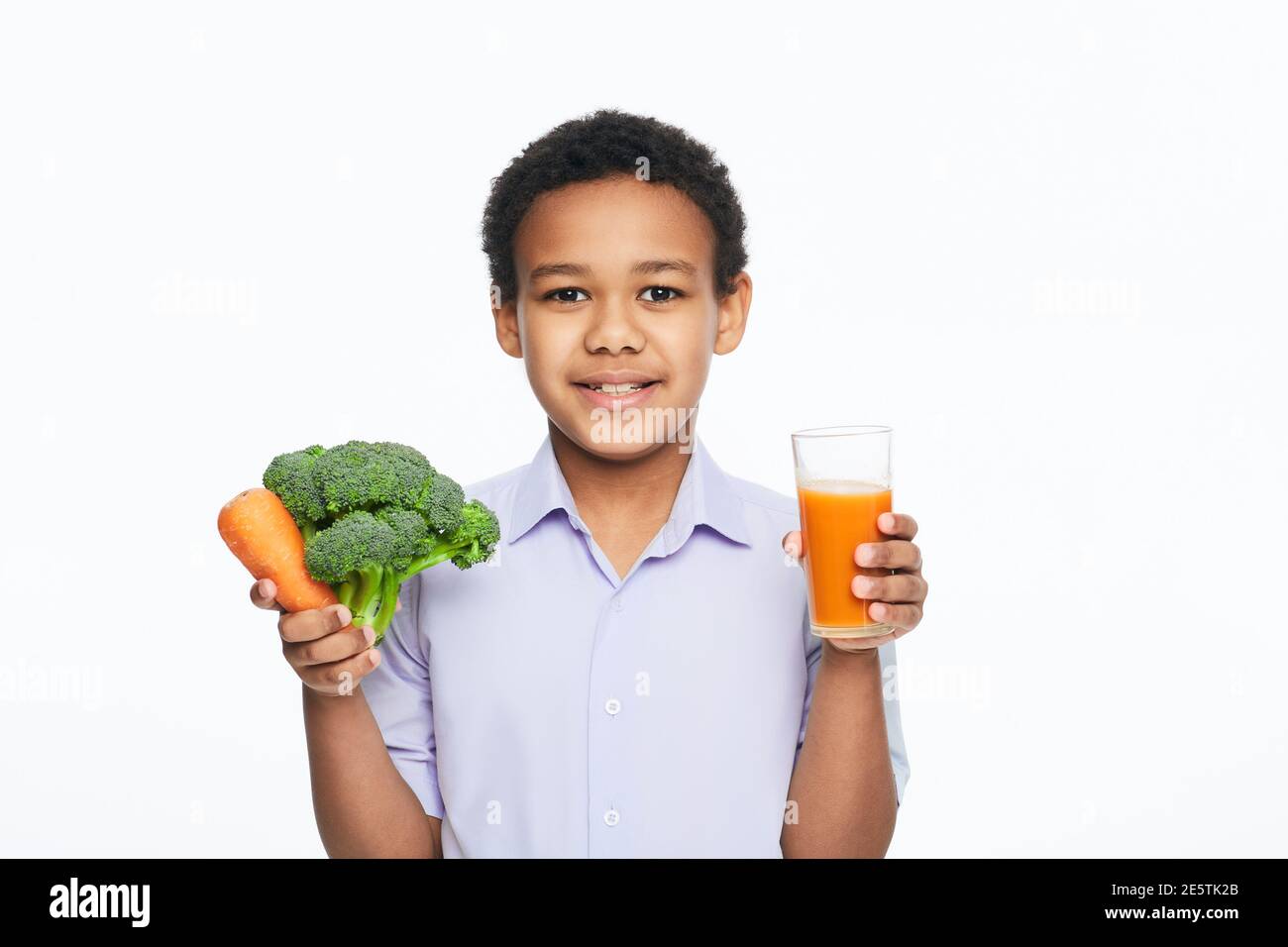 Afroamerikanischer Junge, der Gemüse und frischen Karottensaft in der Hand hält. Gesundes vegetarisches Lebensmittelkonzept für Kinder Stockfoto