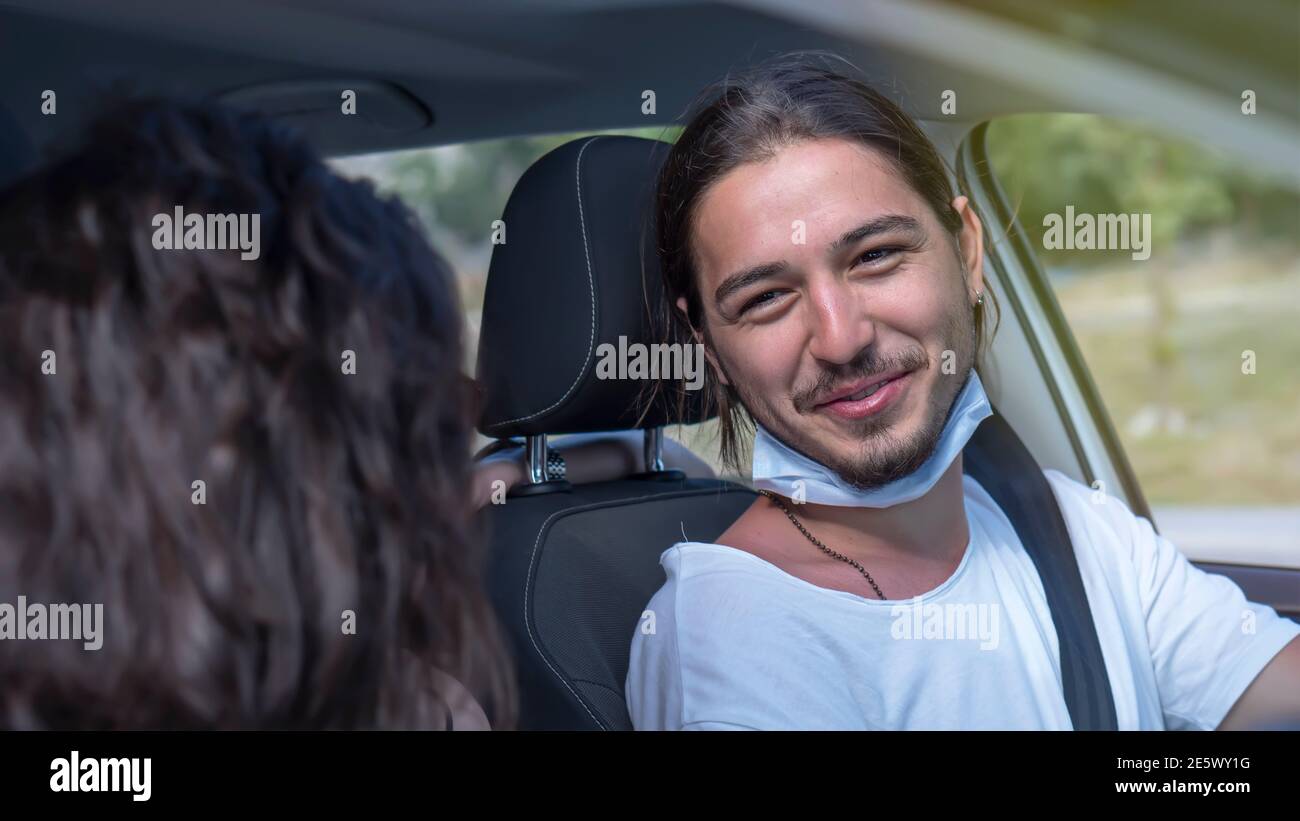 Glückliches junges Paar, Freunde mit Gesichtsmasken sitzen im Auto und reden sich gegenseitig. Roadtrip in neuer Normalität. Corona-Virus-Pandemiekonzept. Stockfoto