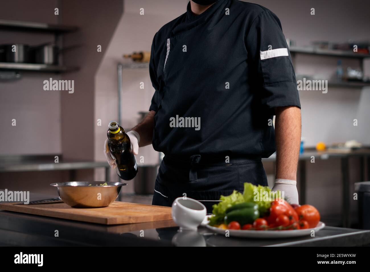 Koch kochen Hände in Handschuhen Zugabe von Olivenöl in griechisch Salat in der Restaurantküche Stockfoto