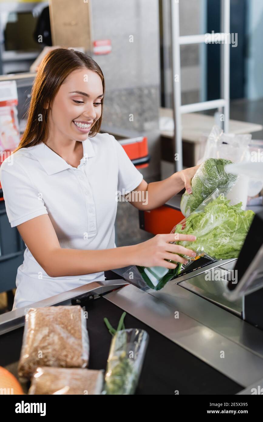 Lächelnder Kassierer hält Gemüse auf Supermarkt Kasse Stockfoto