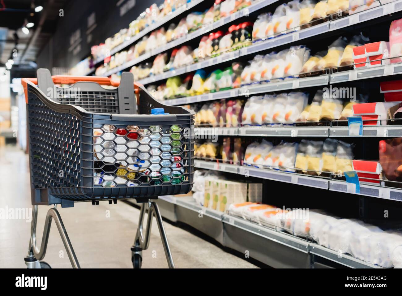 Einkaufswagen in der Nähe von Paketen in Regalen im Supermarkt Stockfoto