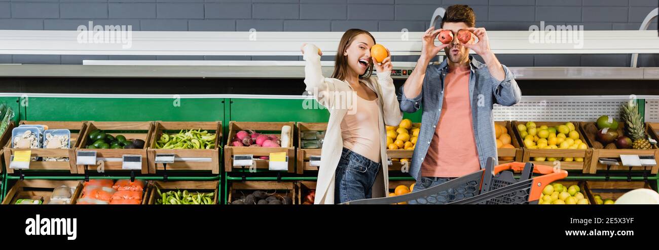Junges Paar hält Früchte in der Nähe Warenkorb im Supermarkt, Banner Stockfoto