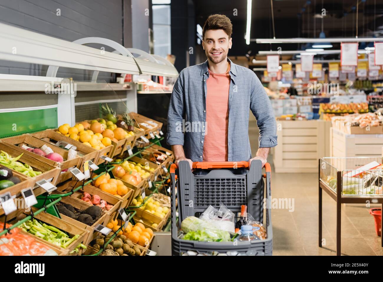 Lächelnder Mann, der in der Nähe des Einkaufswagens im Supermarkt auf die Kamera schaut Stockfoto