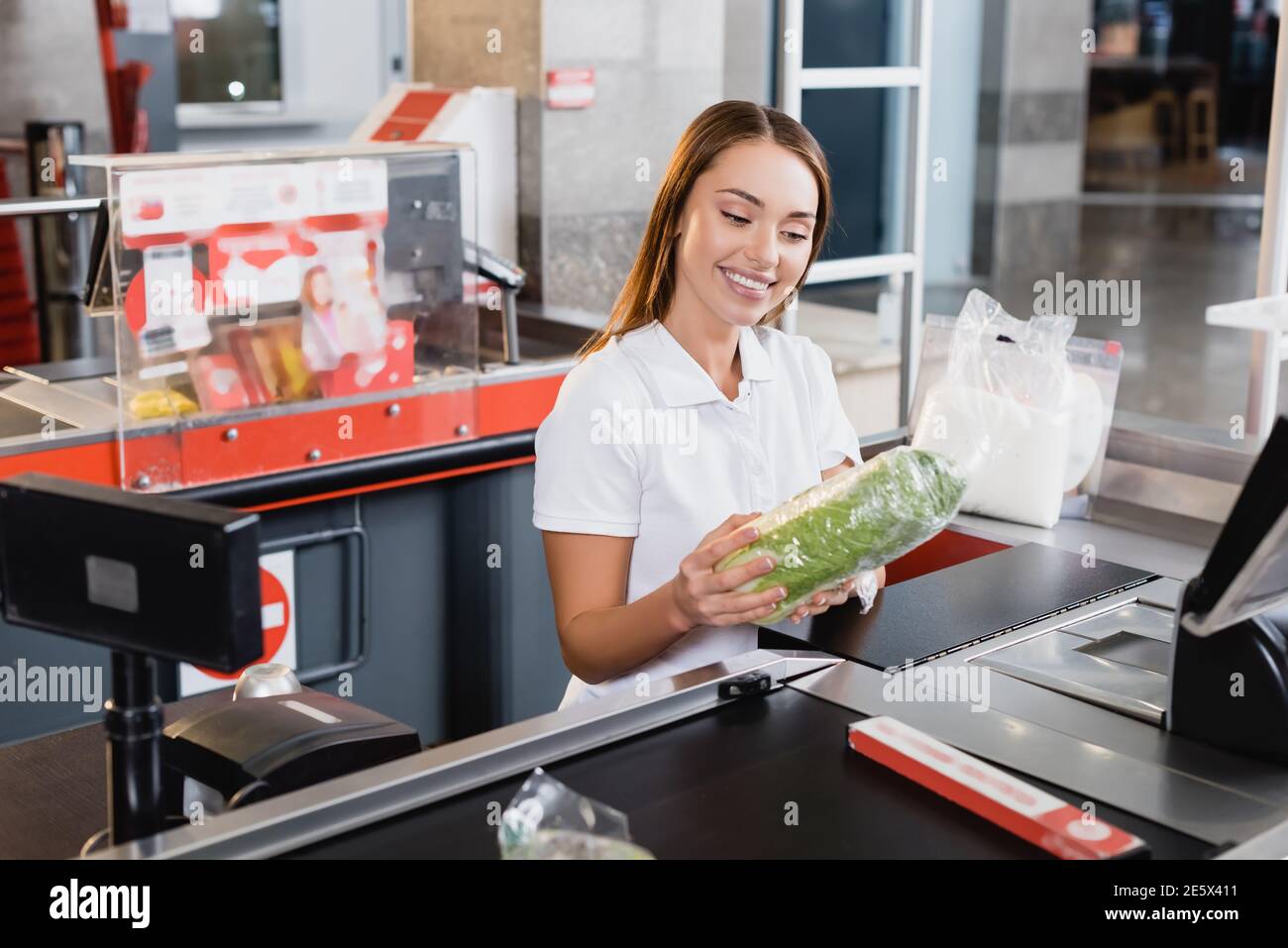 Lächelnder Kassierer mit Salat an der Kasse im Supermarkt Stockfoto
