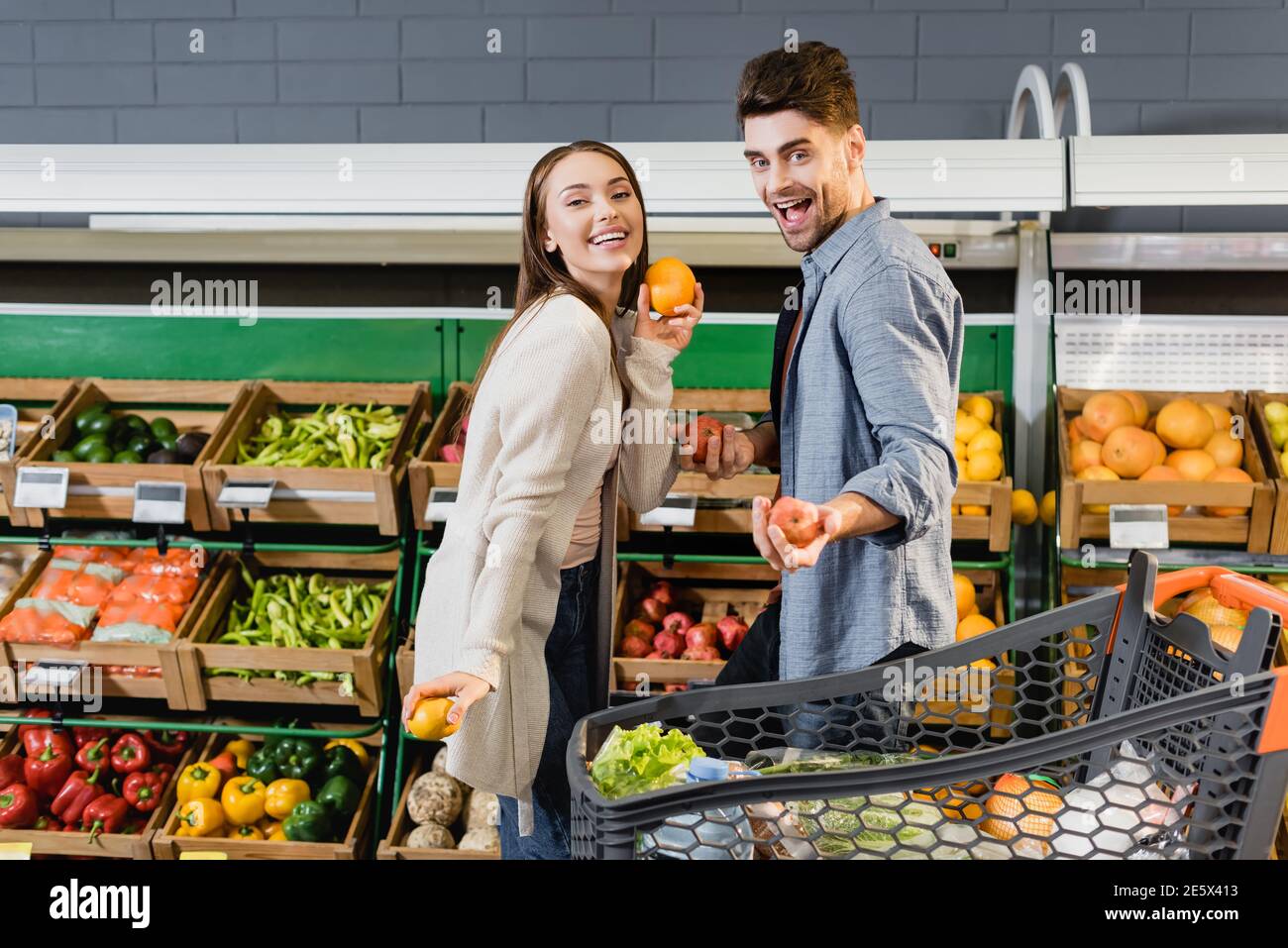 Fröhliches Paar, das Früchte in der Nähe des Einkaufswagens im Supermarkt hält Stockfoto
