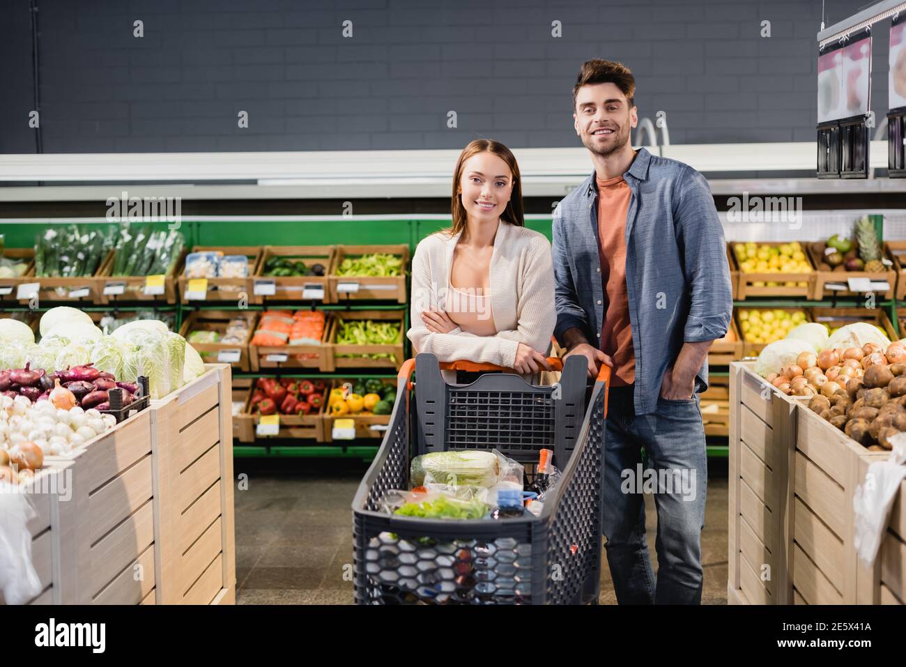 Junges Paar in der Nähe von Einkaufswagen und Gemüse im Supermarkt stehen Stockfoto
