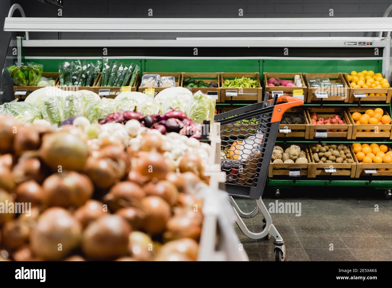 Einkaufwagen neben Gemüse auf verschwommenem Vordergrund im Supermarkt Stockfoto