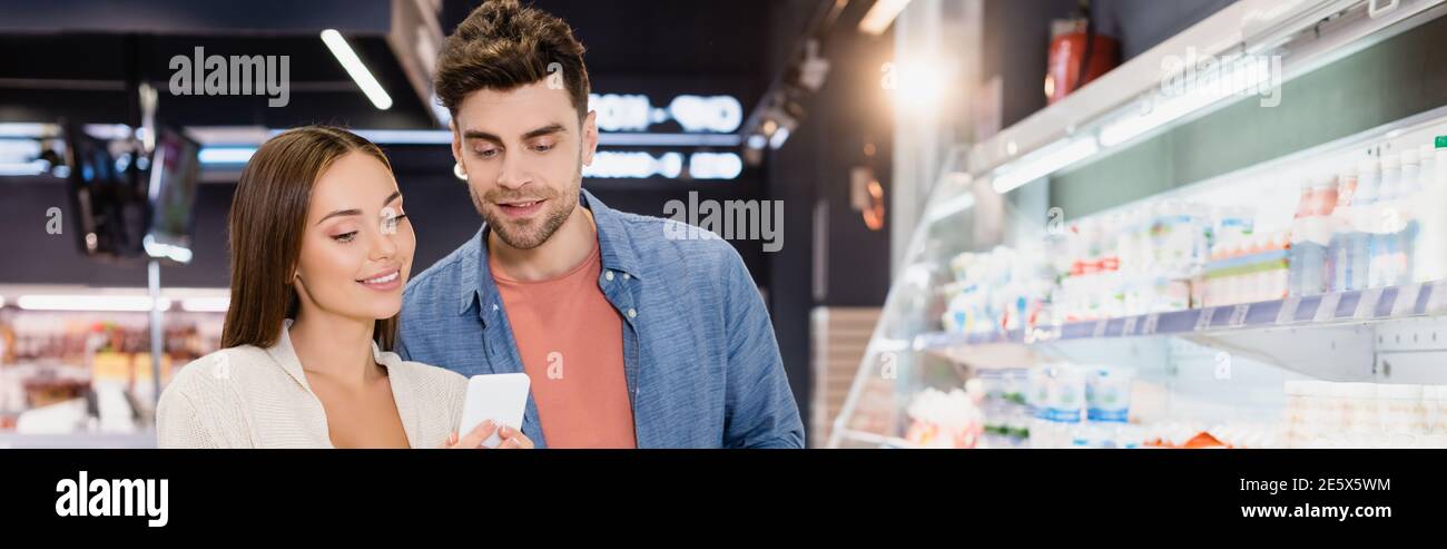 Junges Paar mit Smartphone im Supermarkt, Banner Stockfoto
