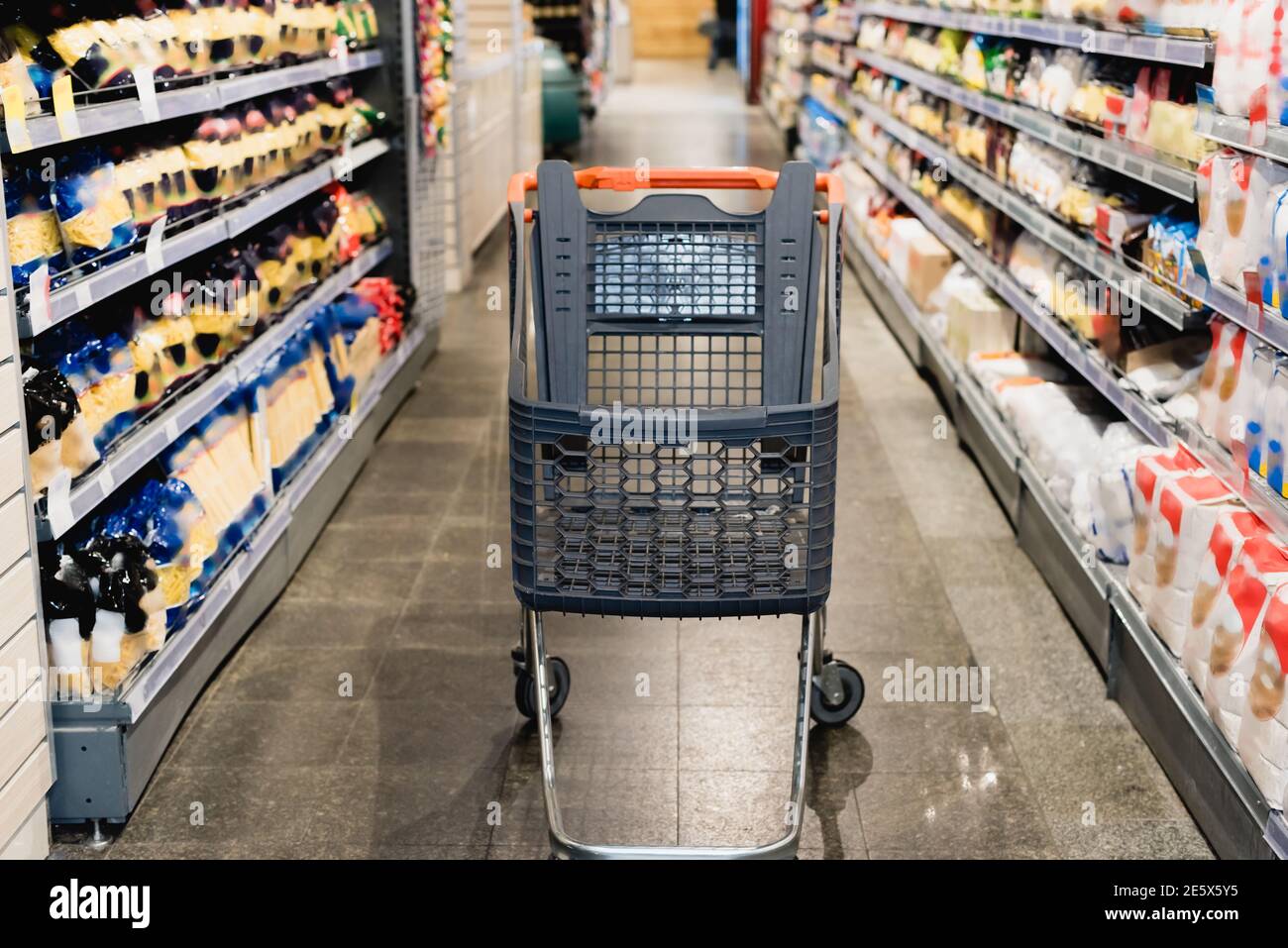 Leerer Einkaufswagen neben Regalen mit Lebensmitteln im Supermarkt Stockfoto