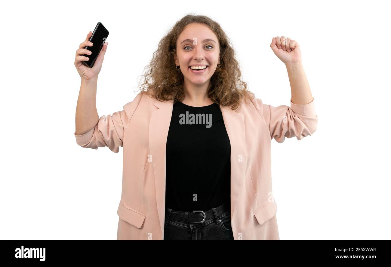 Junge Frau feiert einen Sieg mit ihrem Smartphone in der Hand. Konzept des Gewinnens von Wetten oder Geld online, isoliert auf weißem Hintergrund. Stockfoto