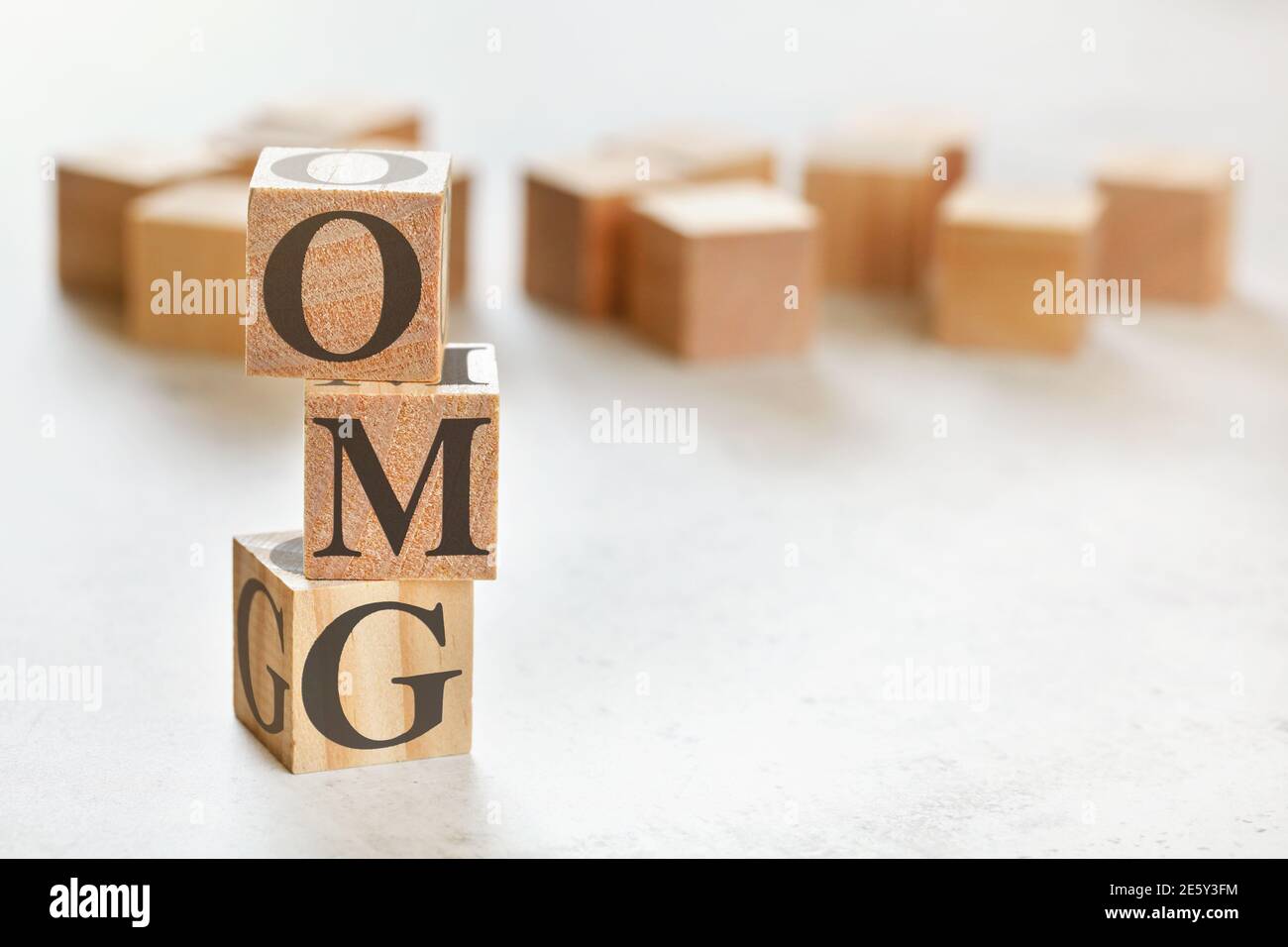 Drei Holzwürfel mit Buchstaben OMG (kurz für Oh my God), auf weißem Tisch, mehr im Hintergrund, Platz für Text in der rechten unteren Ecke Stockfoto