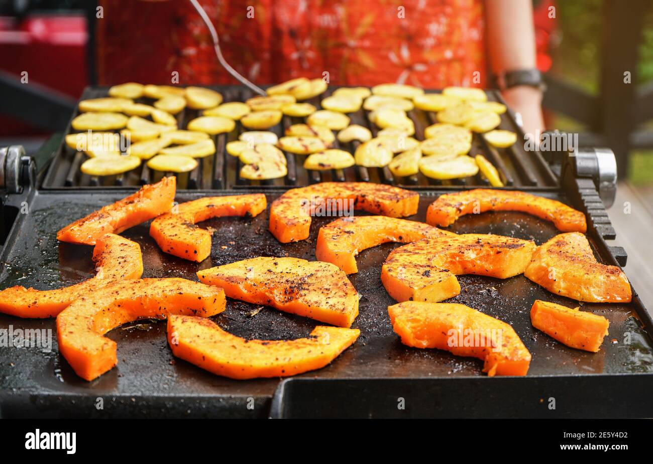Leuchtend orange Butternut Squash Stücke gewürzt mit Gewürzen auf elektrischen Grill gegrillt, verschwommen Kartoffelchips im Hintergrund vorbereitet Stockfoto