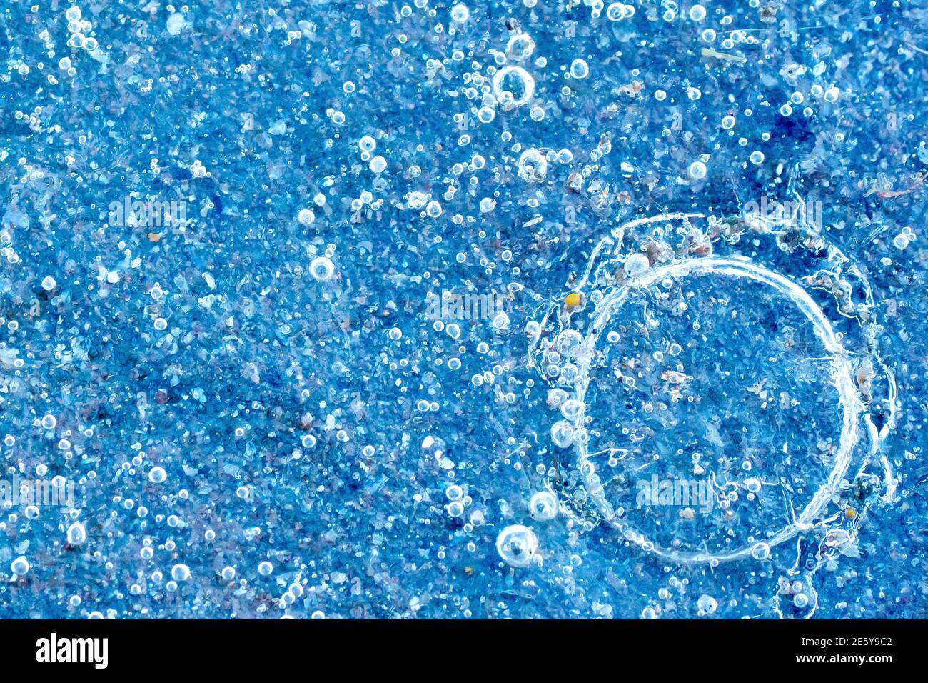 Nahaufnahme von Blasen, die in der gefrorenen eisigen Oberfläche einer Pfütze gefangen sind. Stockfoto
