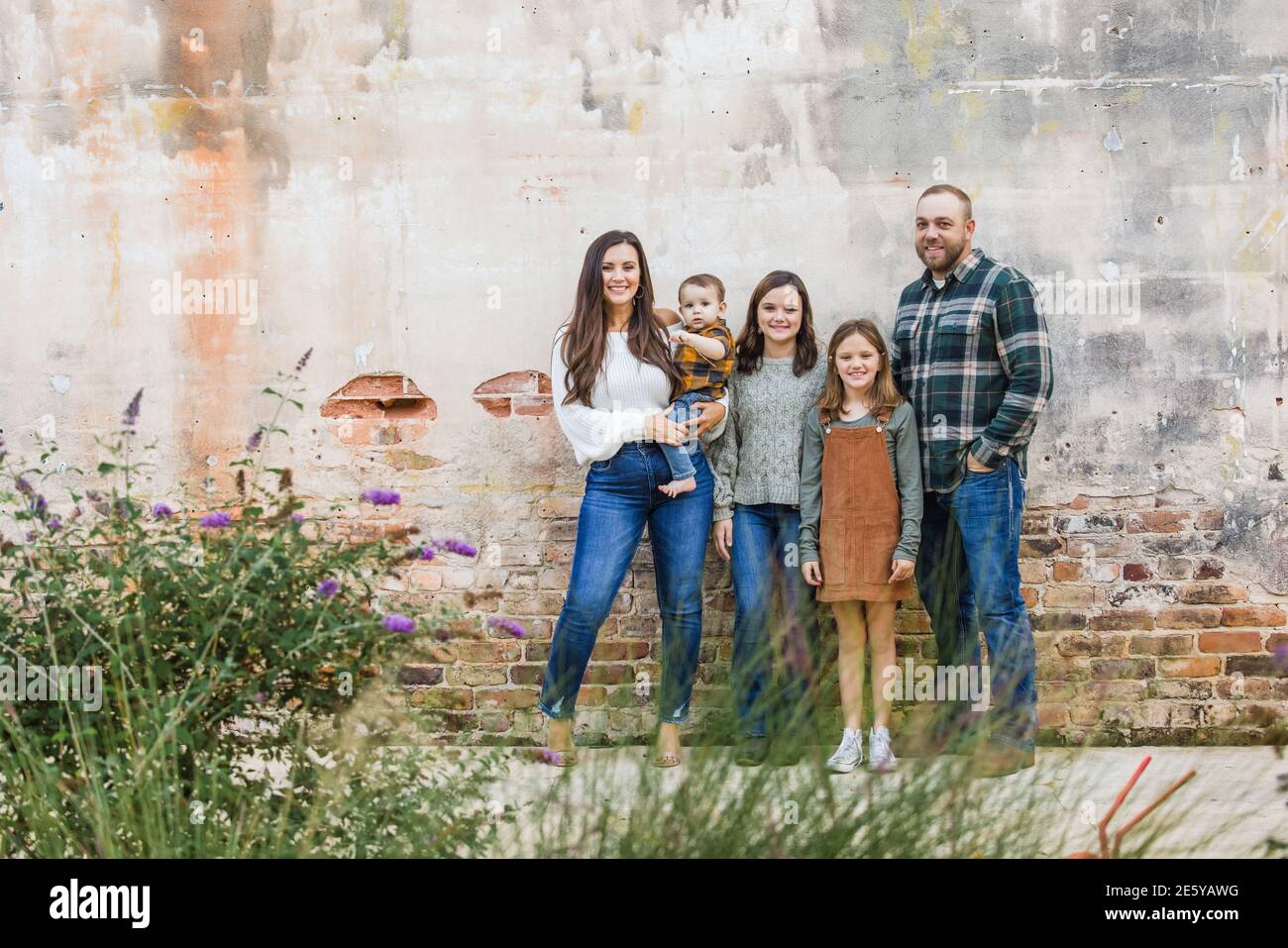 Eine fünfköpfige Familie mit zwei Mädchen und einem Baby Junge, der an einer urbane alte Ziegelmauer steht Stockfoto