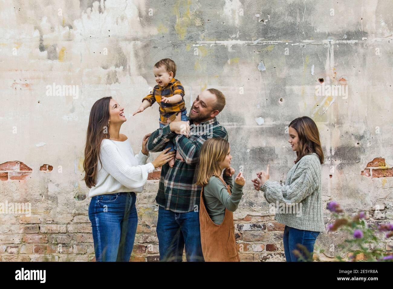 Eine fünfköpfige Familie mit zwei Mädchen und einem Baby Junge, der an einer urbane alte Ziegelmauer steht Stockfoto