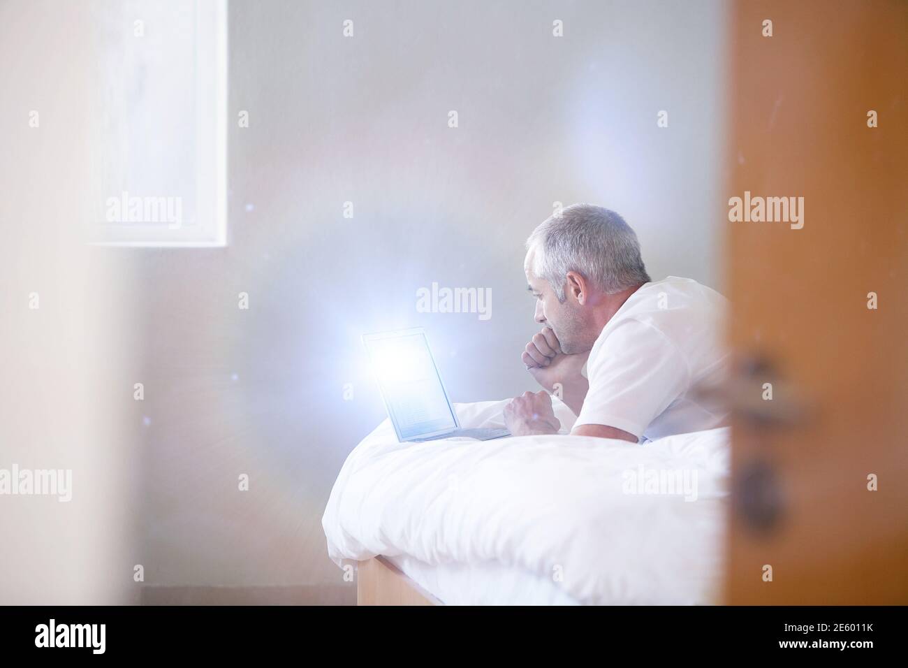 Mann mittleren Alters mit Laptop, während er im Bett lag Zu Hause Stockfoto