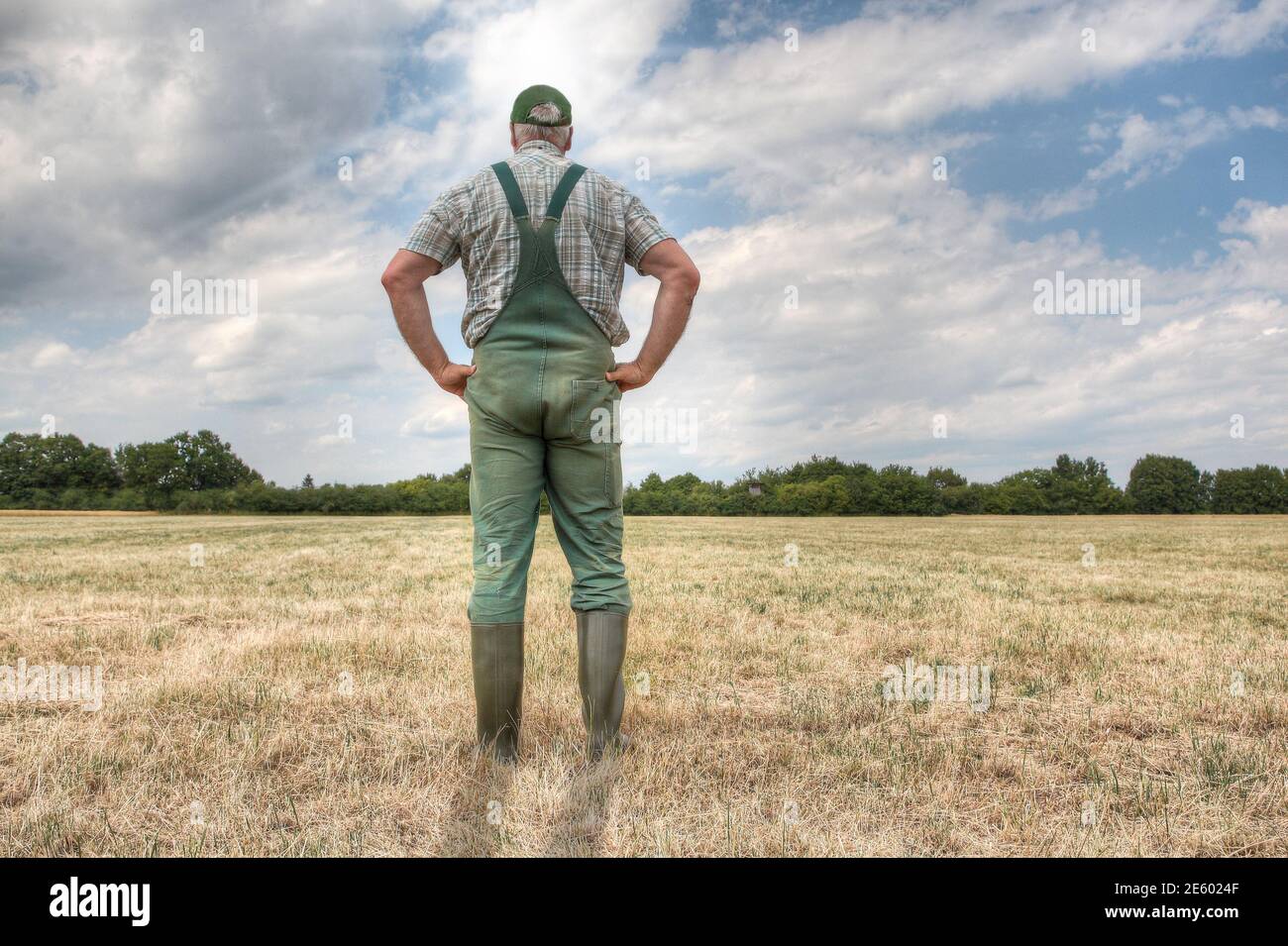 Ein Bauer steht auf seiner ausgetrocknete Wiese und hofft auf Regen, während die Sonne gnadenlos auf seinem Ackerland scheint. Stockfoto