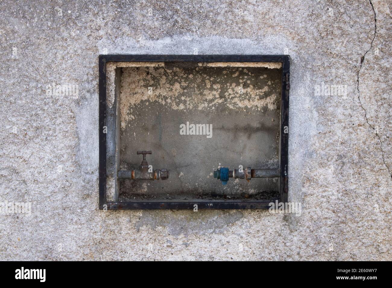 Getrennte Hauswasserleitung mit Wasserhahn und fehlendem Wasser Messgerät an einer externen grungigen Betonwand installiert Stockfoto