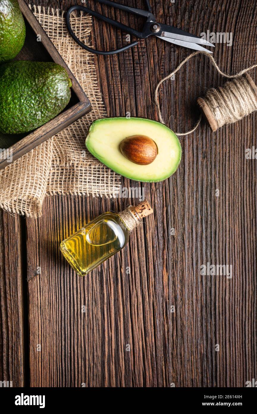 Gesundes Avocado-Öl in einer Glasflasche, verziert mit aufgeschnittener Avocado auf Holzhintergrund mit Kopierraum Stockfoto