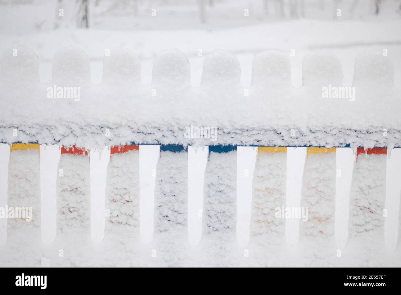 Schneebedeckter mehrfarbiger Zaun aus Holz. Starker Frost, der Spielplatz ist geschlossen. Schnee Stockfoto