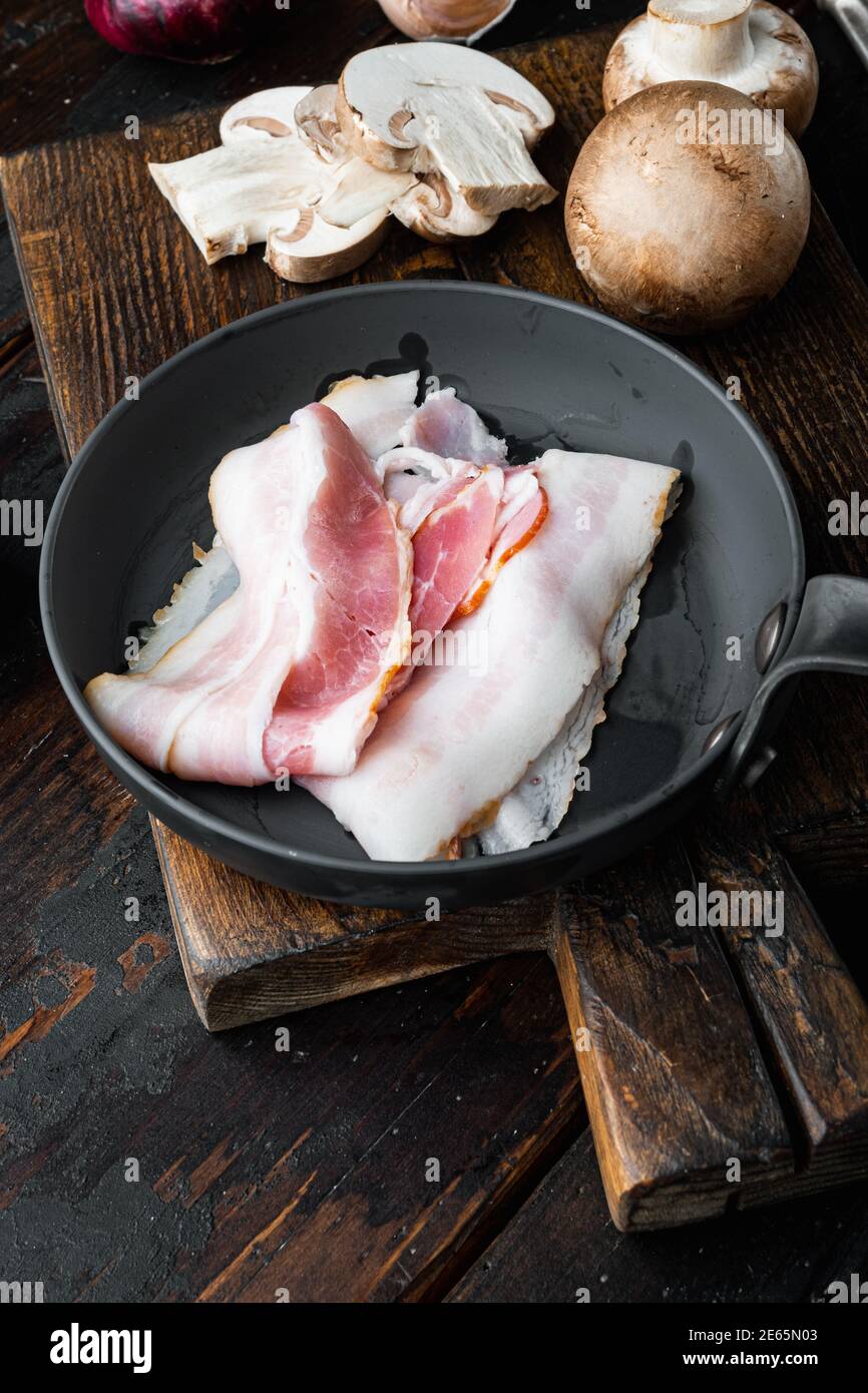 Roher Speck in gusseiserner Bratpfanne, auf altem dunklen Holztisch Hintergrund Stockfoto