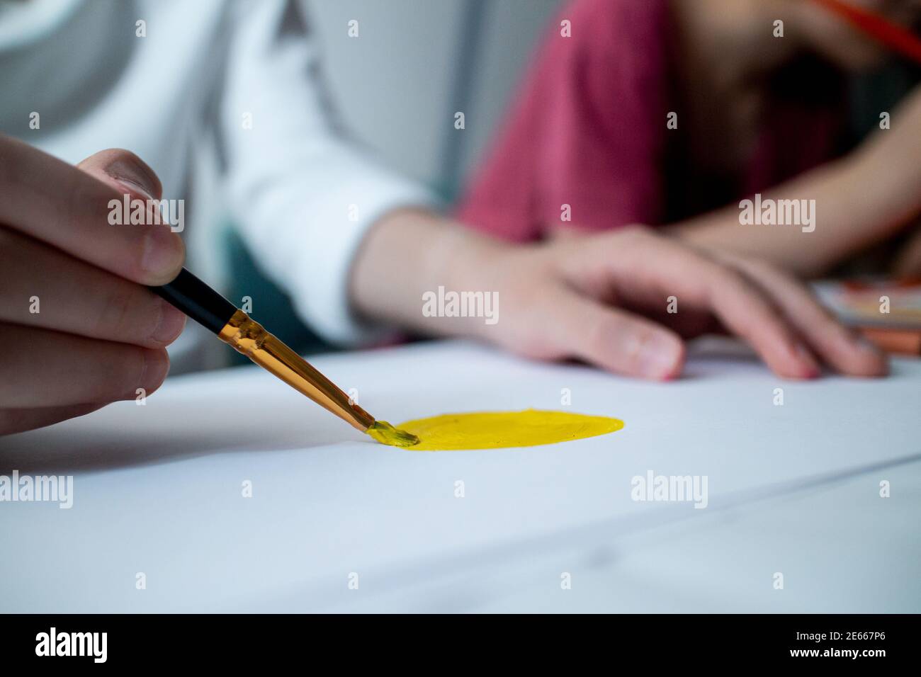 Kinderhand zeichnet gelbe Sonne auf weißes Papier. Zeichenunterricht in der Schule. Schulbildung zu Hause. Art. Nahaufnahme eines Pinsels. Stockfoto