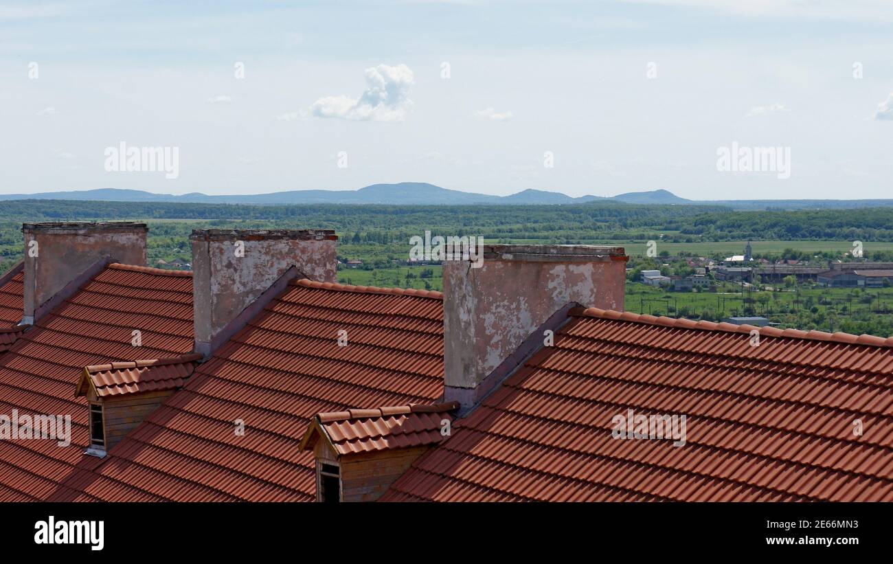 Ziegeldach und alte Kamine Teil des Schlosses Gebäude auf dem Hintergrund des Horizonts, Berge und einsame Wolken Stockfoto