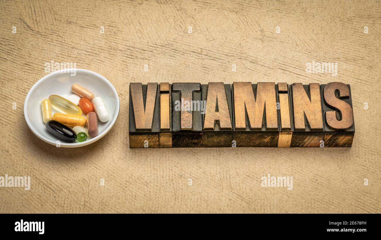 Vitamine Wort abstrakt in Vintage-Buchdruck Holzart mit einer kleinen Schüssel Pillen und Kapseln, gesundes Lifestyle-Konzept Stockfoto