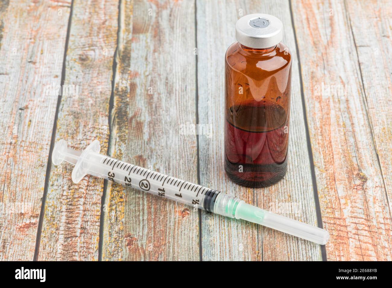 Eine Nahaufnahme einer hygienischen Einweg-Spritze aus Kunststoff mit einem braunen Fläschchen auf einem Holzhintergrund. Stockfoto