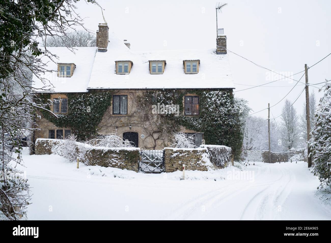 Landstraße und cotswold Steinhütte in Swinbrook im Schnee. Swinbrook, Cotswolds, Oxfordshire, England Stockfoto