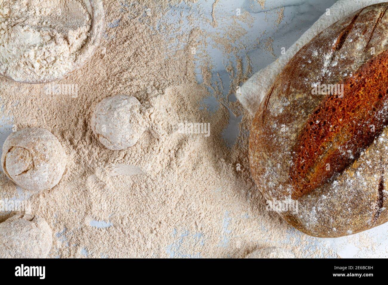 Flaches Bild von einem hausgemachten Sauerteig Brot Laib Kühlung Auf der Serviette auf der Marmorplatte, wo andere Hand gerundet Teig sitzen in Mehl mit Ad Stockfoto