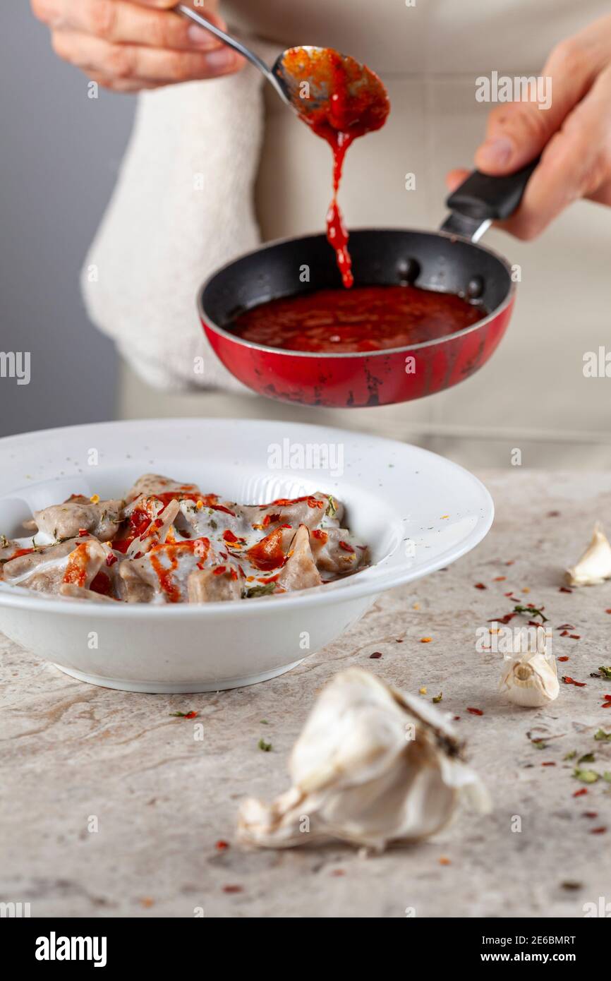 Eine Küchenchefin trägt Schürze fügt frische Tomatensauce zu hausgemachten türkischen Knödel in Joghurt. Dieses traditionelle Gericht ist als Manti bekannt und wird serviert Stockfoto
