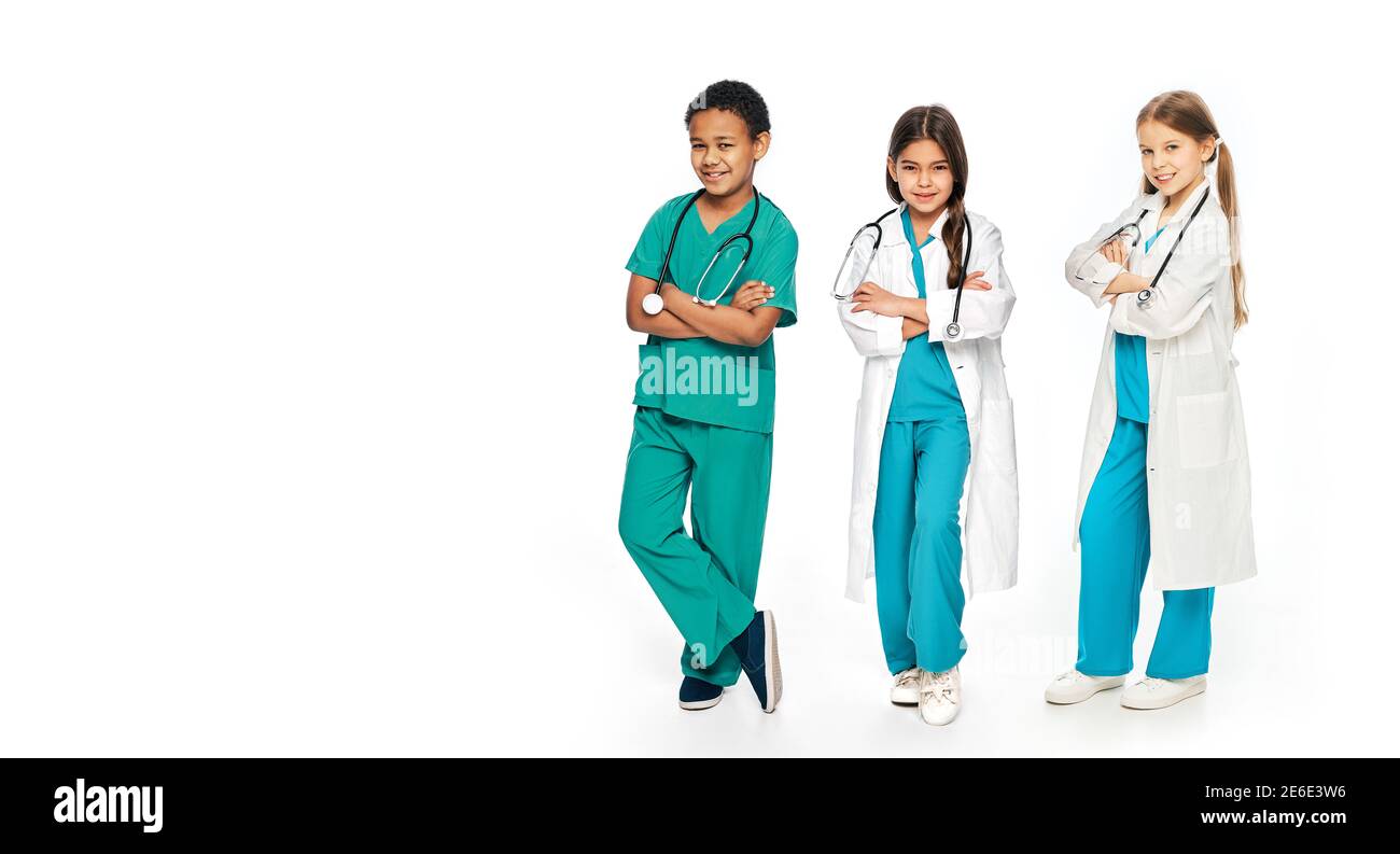 Gruppe von positiven multiethnischen Kindern tragen medizinische Uniformen, in voller Länge. Konzept der zukünftigen Ärzteberuf Stockfoto