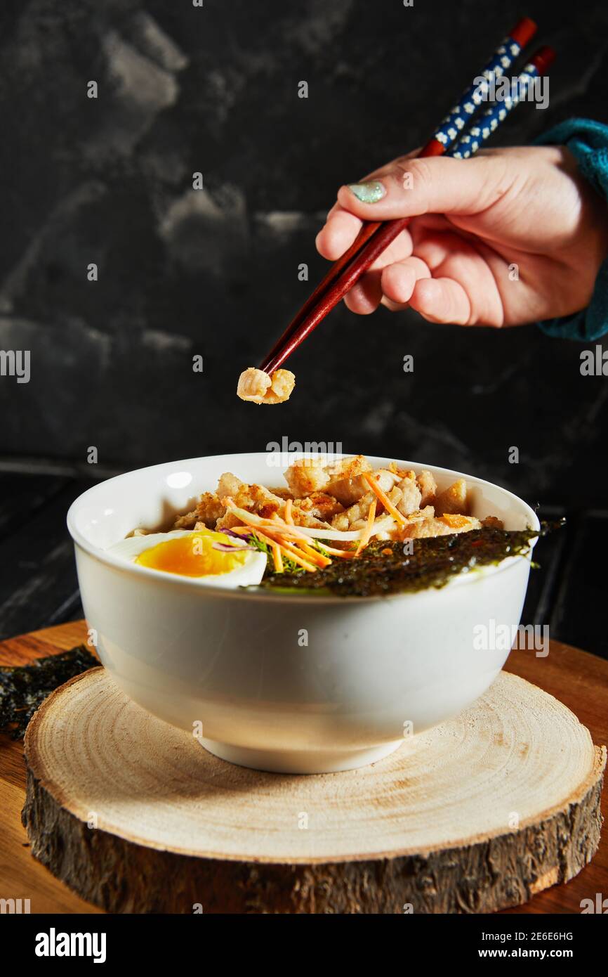 Junge Japanerin beim Abendessen schmeckt köstlich udon Ramen - japanische Ramen-Suppe mit Huhn, Ei, Knoblauch und Nudeln auf dunklem Holzgrund Stockfoto
