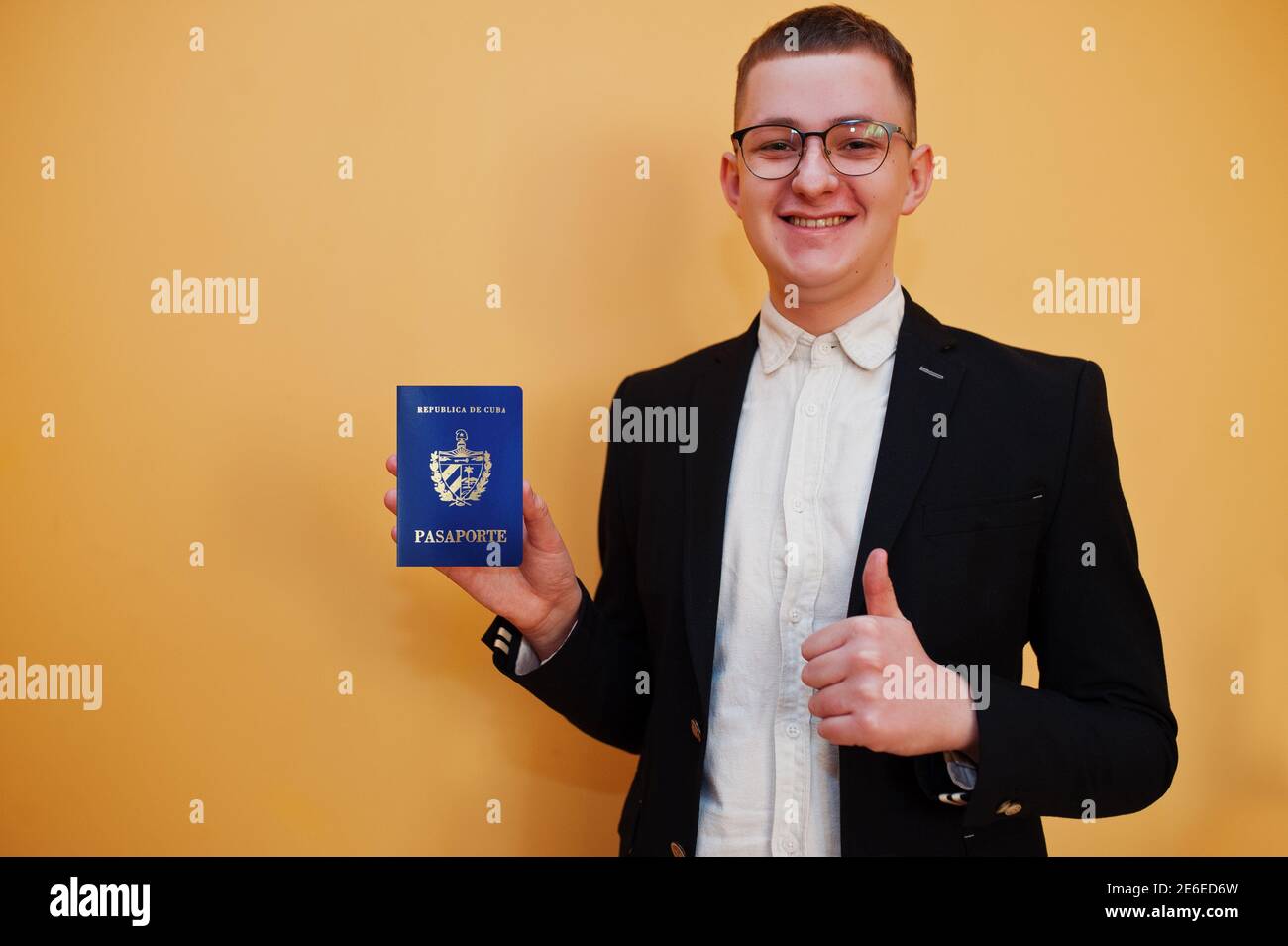 Junger, hübscher Mann mit ausweis der Republik Kuba auf gelbem Hintergrund, glücklich und zeigt Daumen hoch. Reisen Sie nach Amerika Länder. Stockfoto