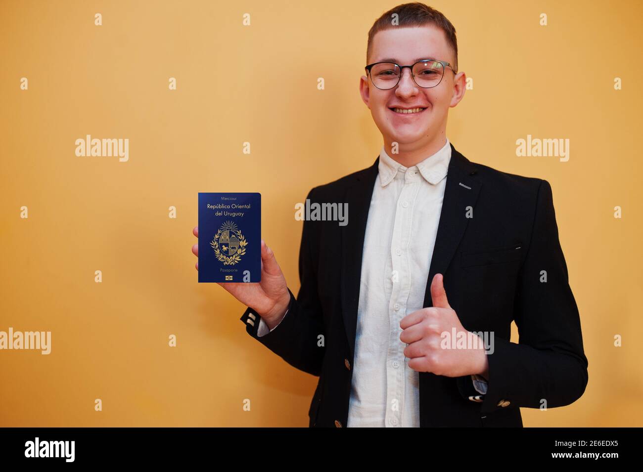 Junger, hübscher Mann mit ausweis der Orientalischen Republik Uruguay auf gelbem Hintergrund, glücklich und zeigt den Daumen hoch. Reisen Sie nach Amerika Länder. Stockfoto