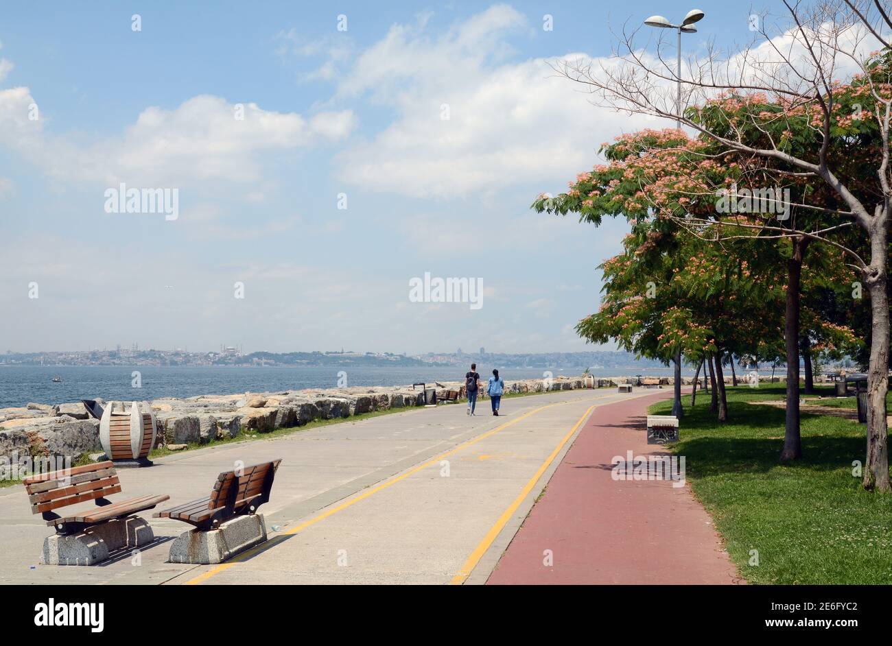 Ein paar Leute, die durch einen Park am Wasser in Moda, Istanbul mit der alten Skyline in der Ferne laufen. Stockfoto