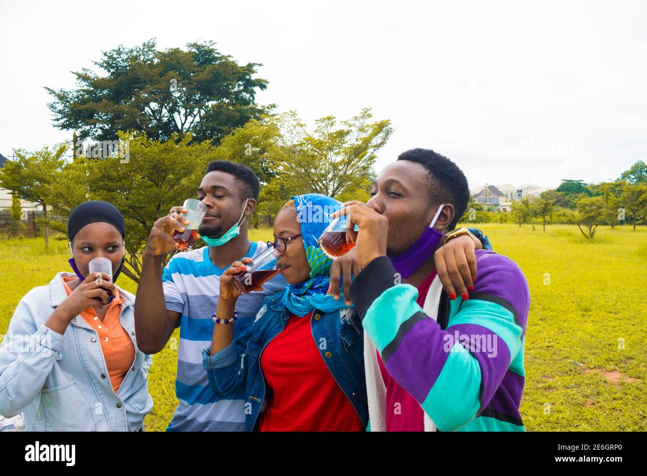 Junge schwarze Menschen stehen in einem Park und trinken aus Ihre Glasplatten Stockfoto