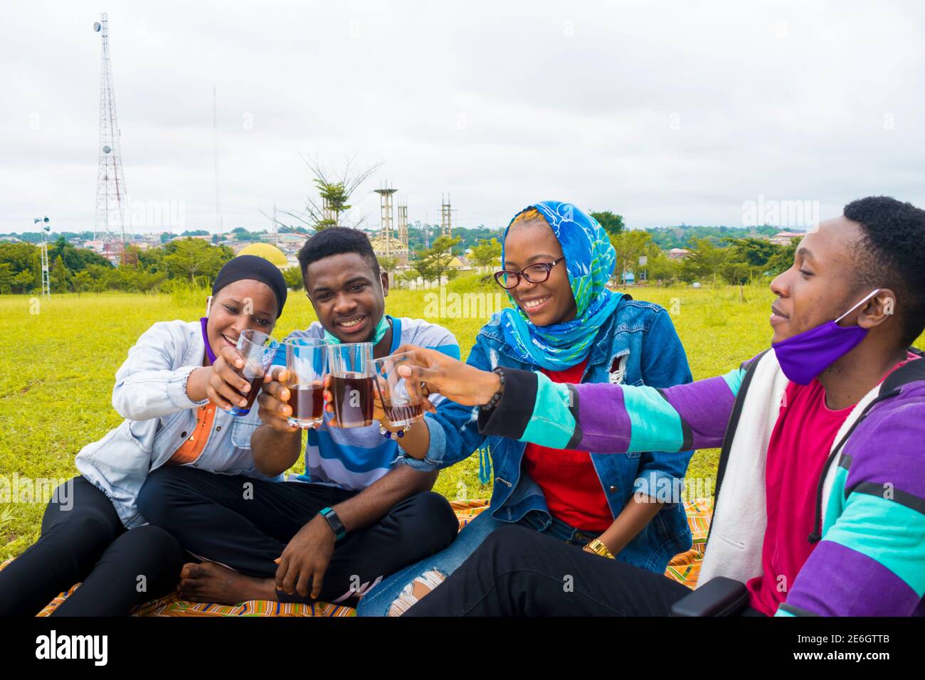 Junge schwarze Menschen sitzen in einem Park und machen ein Toast mit Getränk in den Tassen Stockfoto