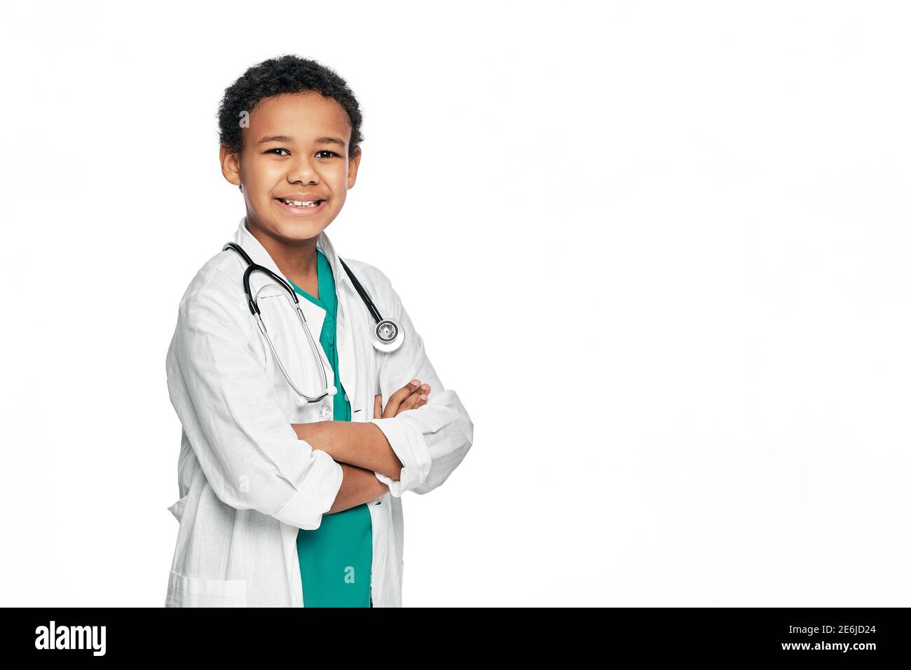 Lächelnder afroamerikanischer Junge, der einen Arztmantel mit gekreuzten Armen trägt, posiert und in die Kamera schaut. Kind, zukünftiger Arzt Stockfoto