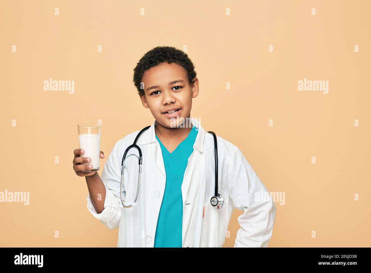 Vorteile von Milch für Kinder. Afroamerikanisches männliches Kind, gekleidet wie ein Arzt, der ein Glas Milch hält Stockfoto