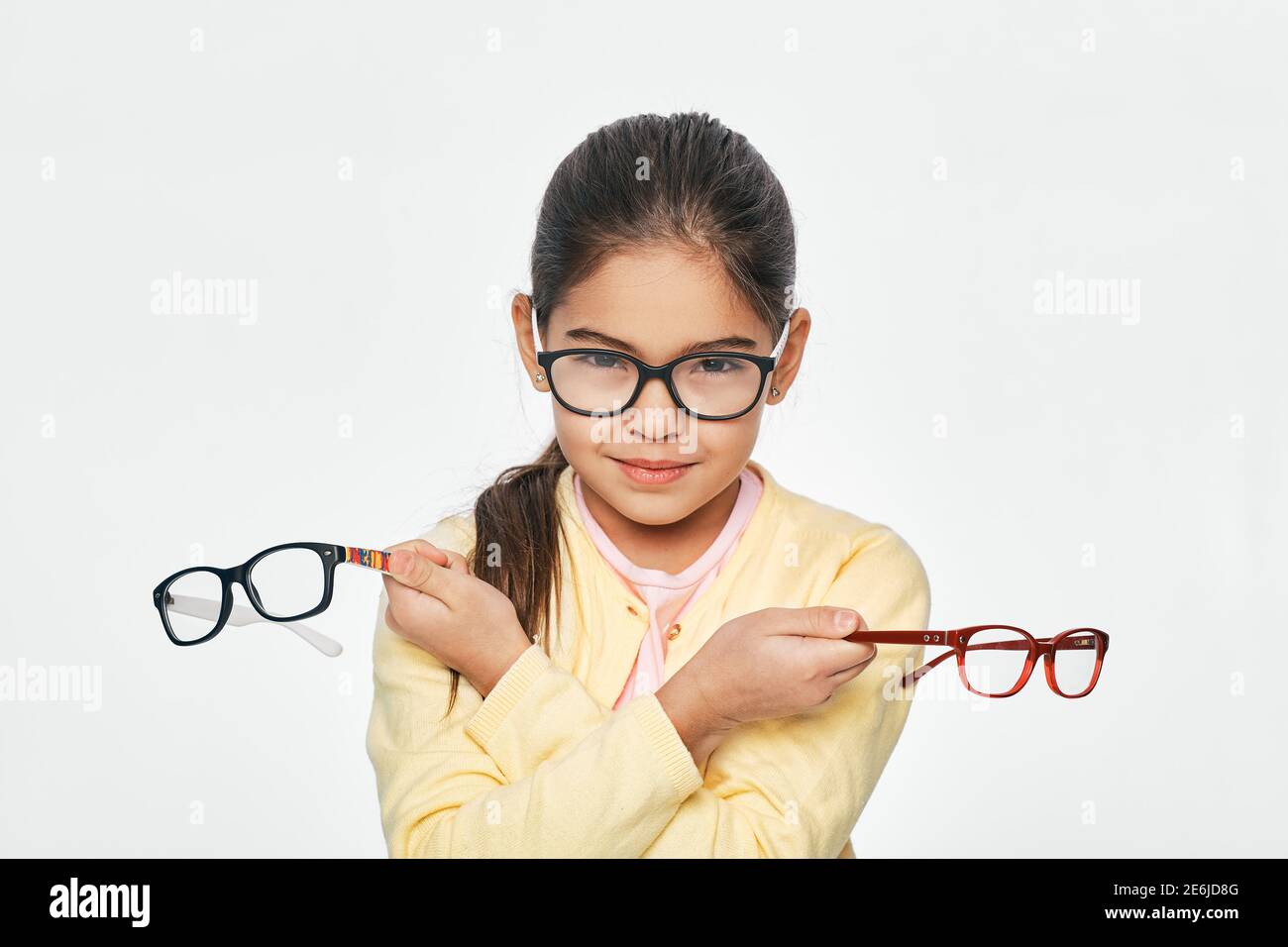 Schöne lateinamerikanische kleine Mädchen hält viele stilvolle Brillen in den Händen, für Sehkorrektur für Kinder. Isoliert auf Weiß Stockfoto