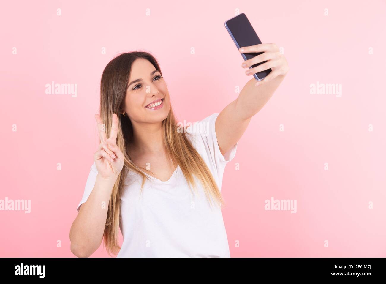 Eine junge blonde Frau macht ein Selfie mit ihrem Handy Telefon macht eine Siegesgeste Stockfoto